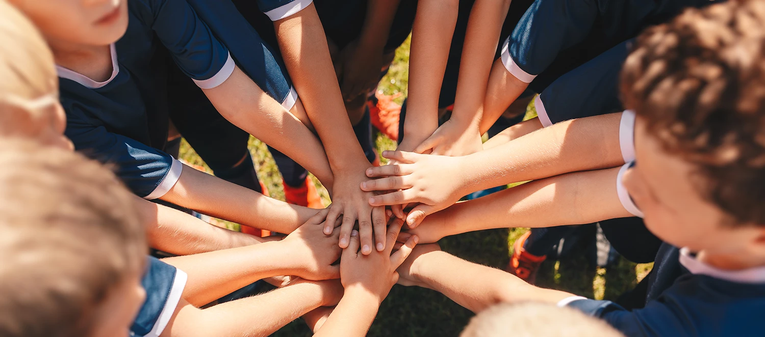eine Gruppe Kinder in Trikots steht im Kreis und legt die Hände zusammen